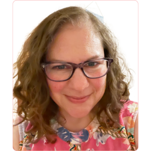 Nadia Arbach portrait photo showing Nadia wearing a pink top and blue glasses.
